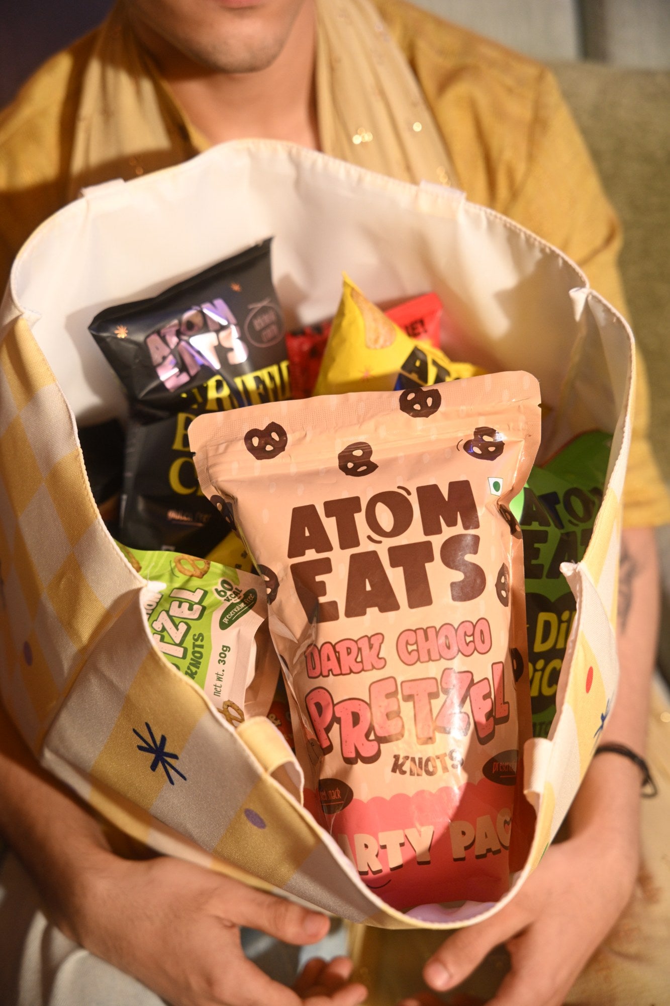 Friends in festive wear holding Atom Eats gift boxes, tote and snack packs